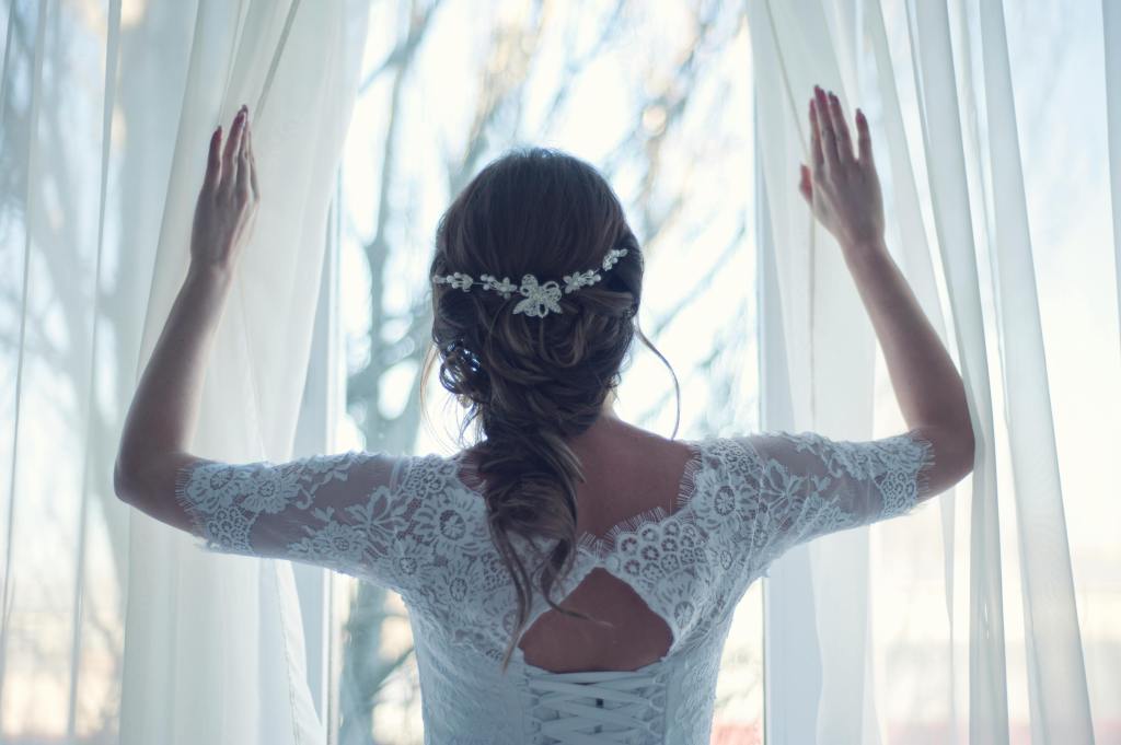 Bride in wedding dress looking out window 