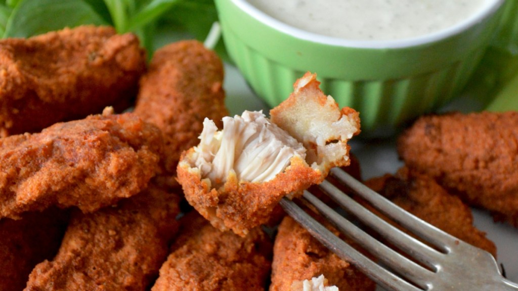 Close up of a plate of chicken nuggets next to a small bowl of ranch. One of the nuggets has been bitten in half and is on a fork