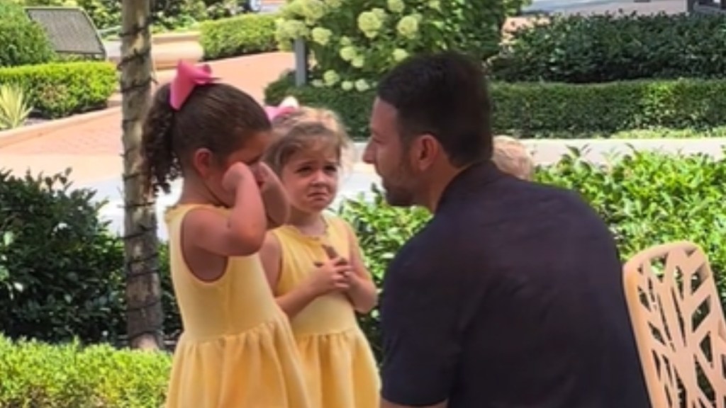 Two little girls and their dad chat outside. Dad is on their level, looking calm. Both girls are crying and ones rubs her eyes