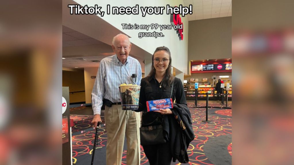 A young woman standing next to her grandpa in a movie theater lobby.