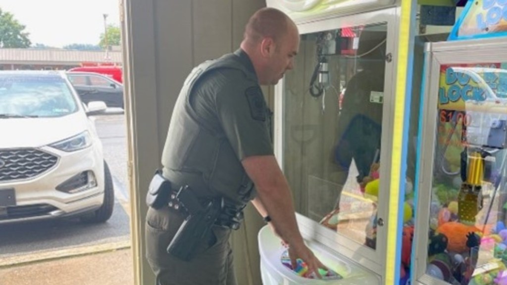 An officer concentrates as he leans against a claw machine, seemingly about to play