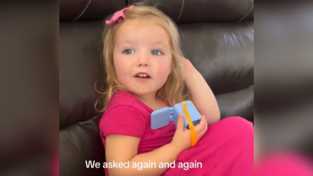 A little girl in a pink dress sitting on a couch.