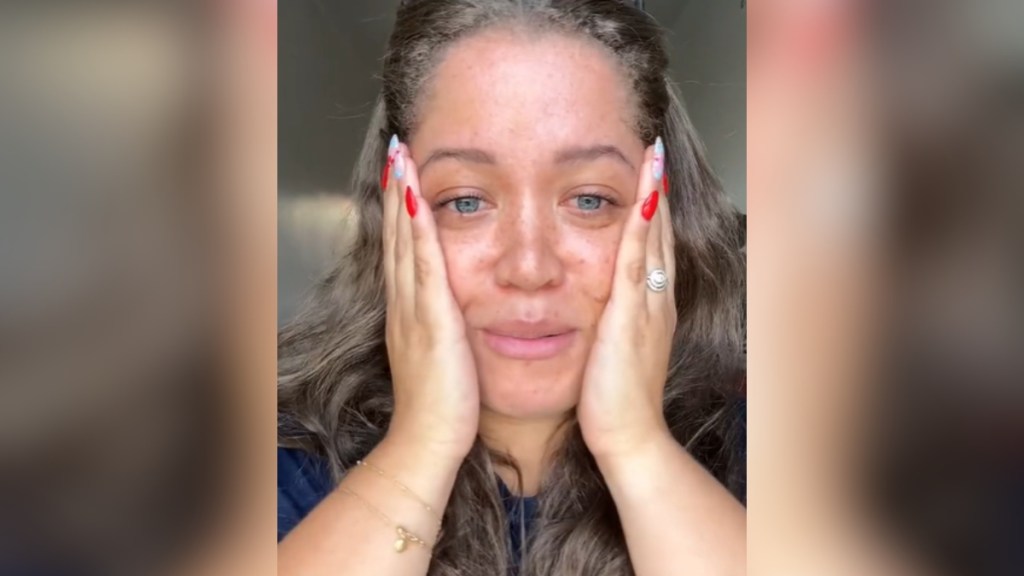 Close up of a woman on the verge of tears. She holds both of her hands up to her cheeks.