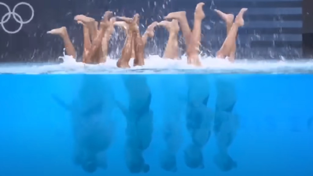 Olympic swimmers are upside down in the pool, feet above the water