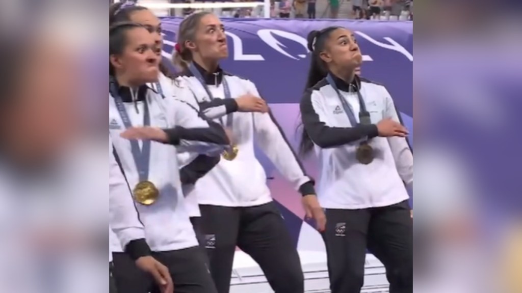 Three women on the New Zealand women's rugby team hold up their arms across their chests as they perform the Haka at the Olympics