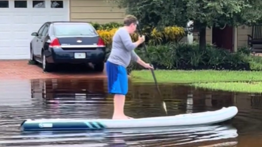 Side-view of a woman on a paddleboard on a flooded road