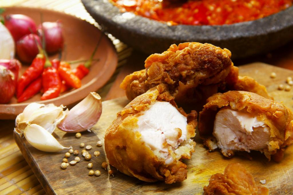 Three chicken nuggets on a wood cutting board. Nearby is a container with peppers and onions. Another container appears to have salsa