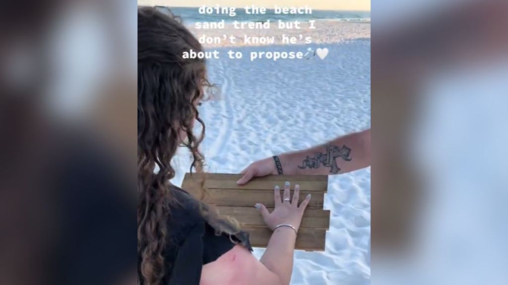 A woman at the beach placing her hand on a wooden board.