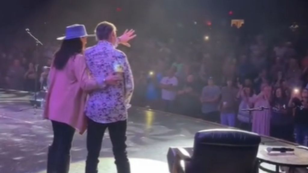 Randy Travis is assisted on stage while the crowd cheers.