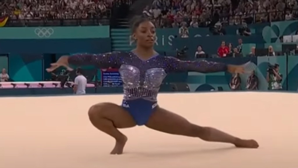 Simone Biles squats, one leg out, as she does her floor routine at the Paris Olympics