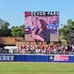 View of a large screen at a softball game. The screen shows Krystal Keith, Toby Keith's daughter, singing