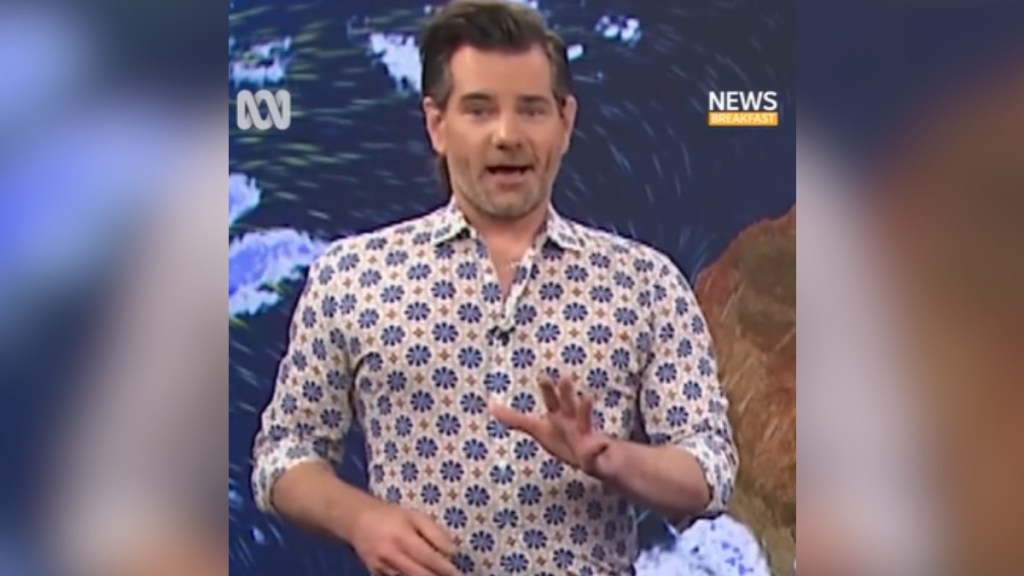 Close up of a weatherman talking, his hand raised as he speaks