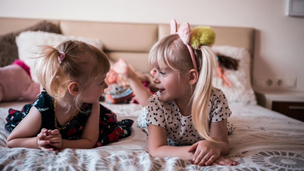 Stock images shows two sisters lying on a bed talking about costumes.