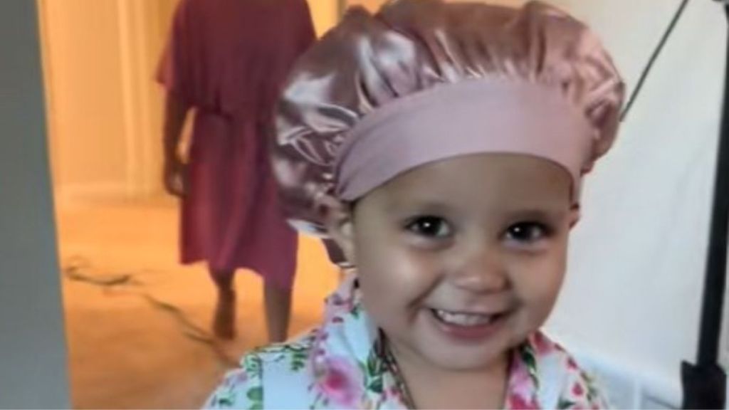 Image shows a toddler wearing a traditional sleep bonnet and giggling.