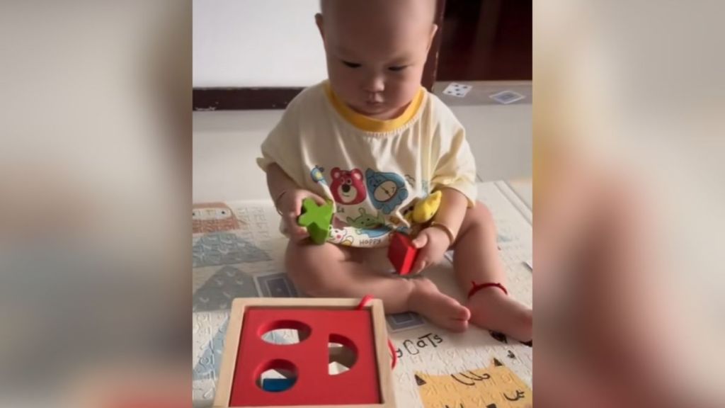 A baby holding different shapes while looking at a puzzle toy.