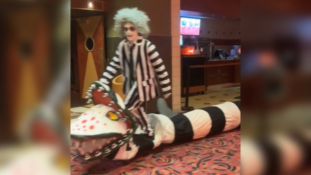 Man dressed as Beetlejuice rides on a "sandworm" through a movie theater.