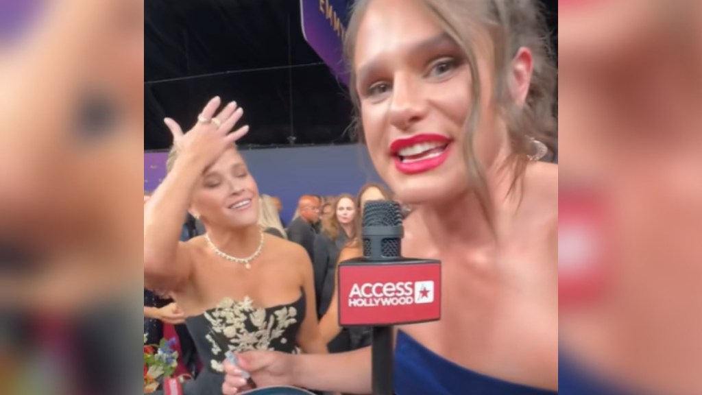 Ilona Maher looks at the camera as she holds a mic and interviews Reese Witherspoon who has her eyes closed, one hand on her forehead like she's frustrated