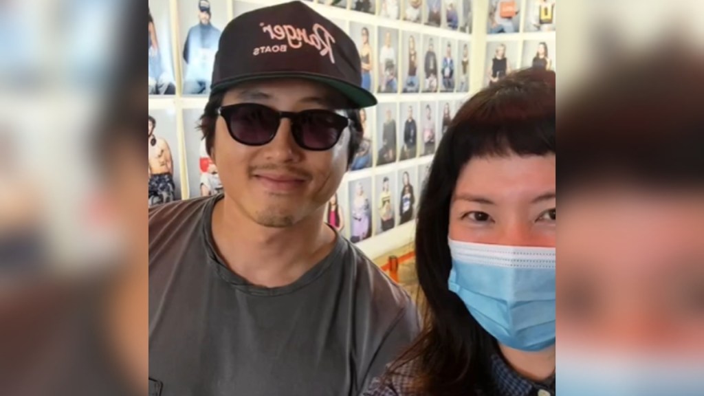 A man and woman pose in front of a wall full of photos at a coffee shop