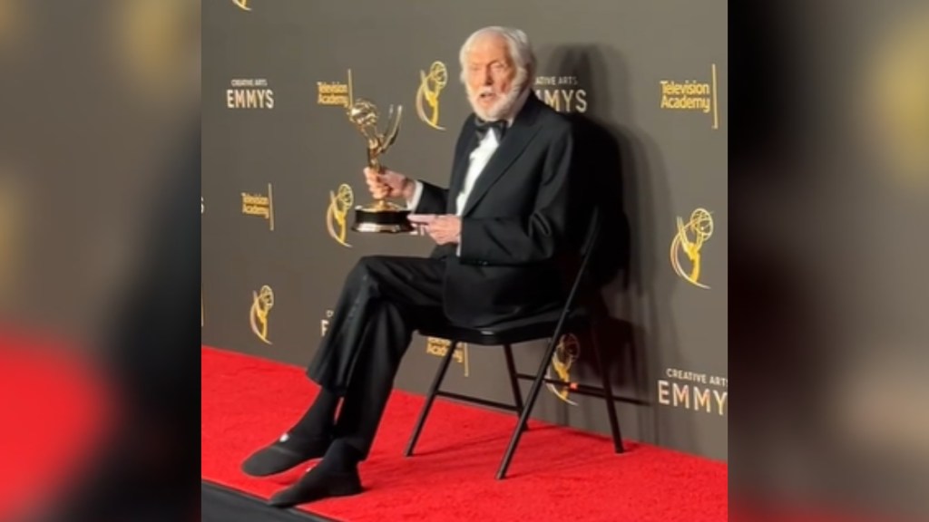 Dick Van Dyke sits on a chair on the Emmys' red carpet. He talks as he points to the Emmy in his hand