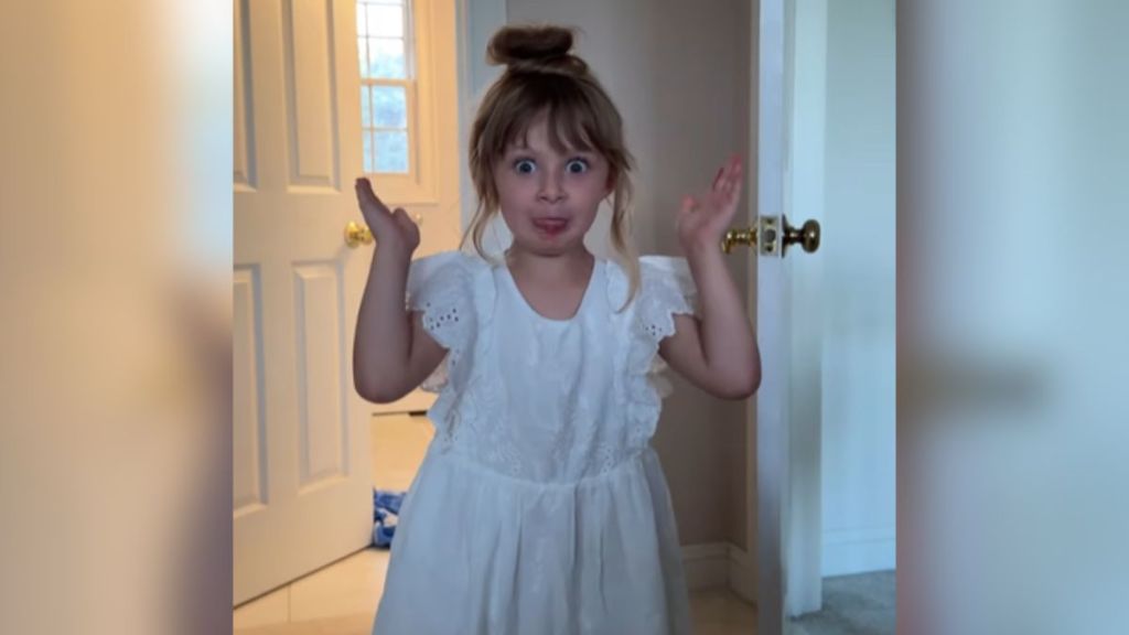 A little girl in a white dress making a silly face.