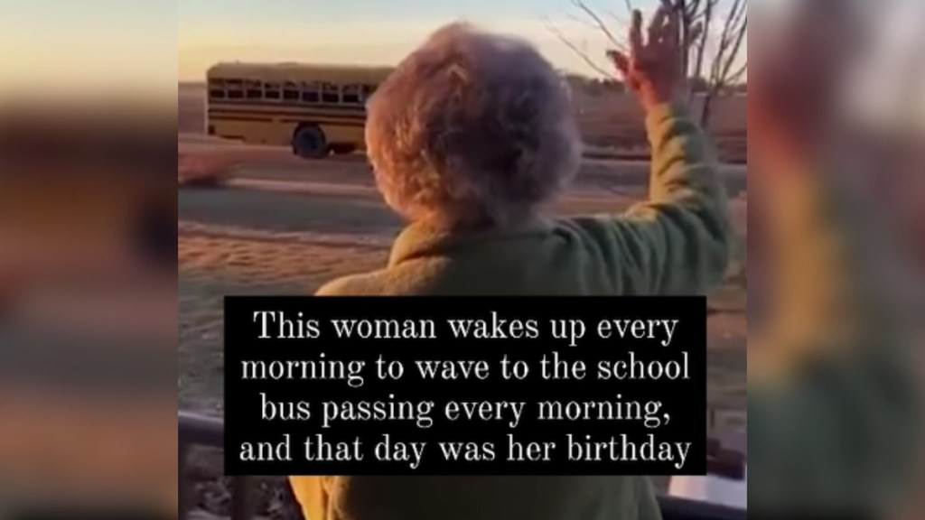 View from behind of a grandma standing outside as she waves at the school bus passing by from a distance