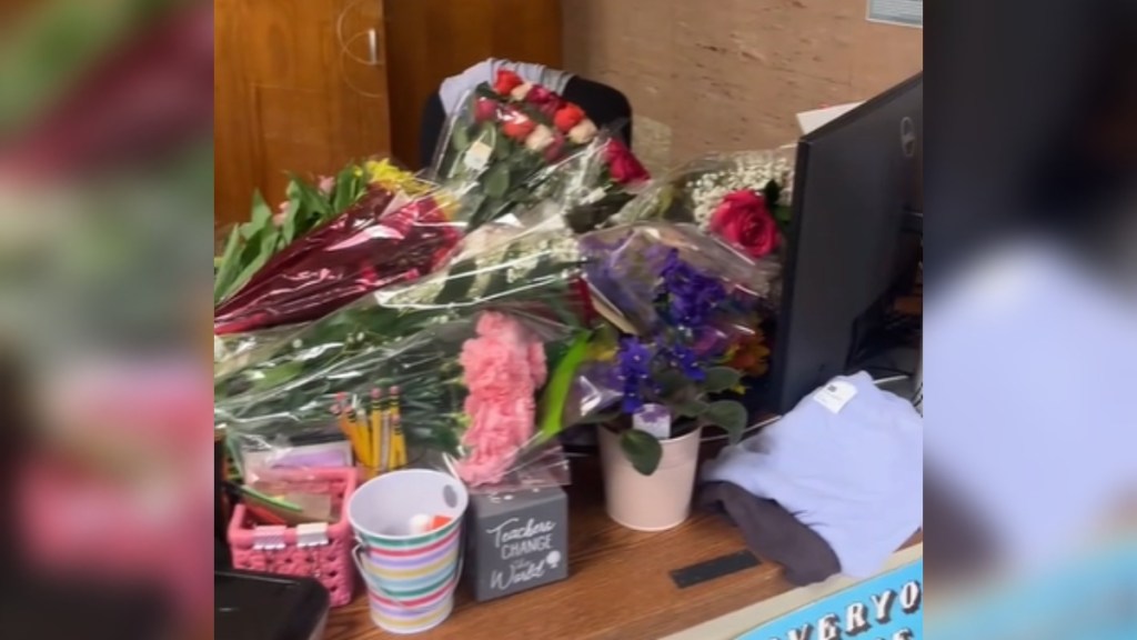 A teacher's desk is full of flowers and other colorful items