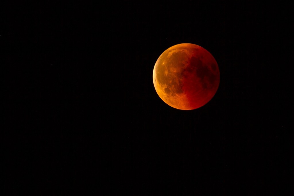 View of a reddish full moon surrounded by a dark sky