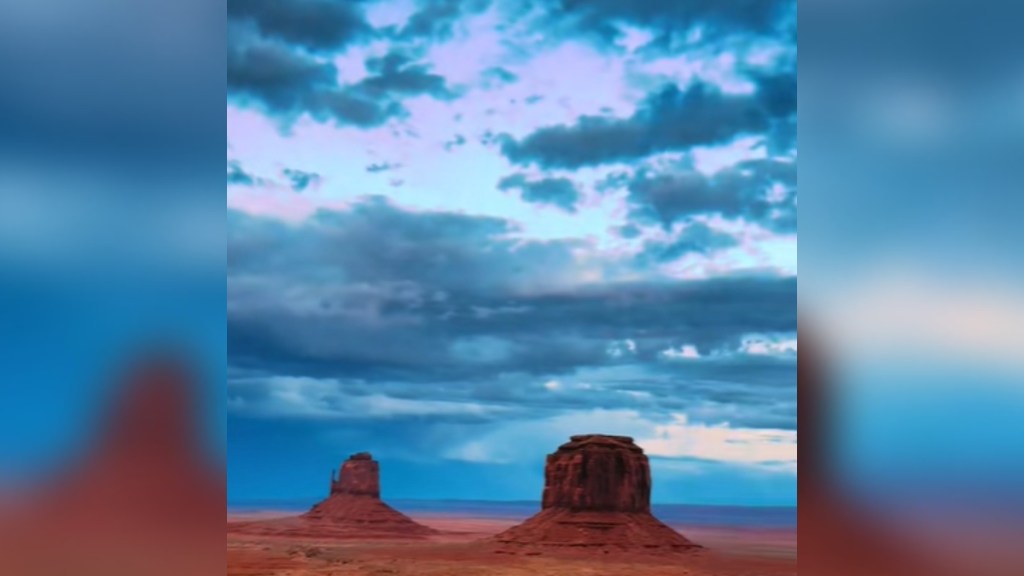 View of Monument Valley as a storm starts to roll in. The sky is various shades of blue and there's lots of clouds