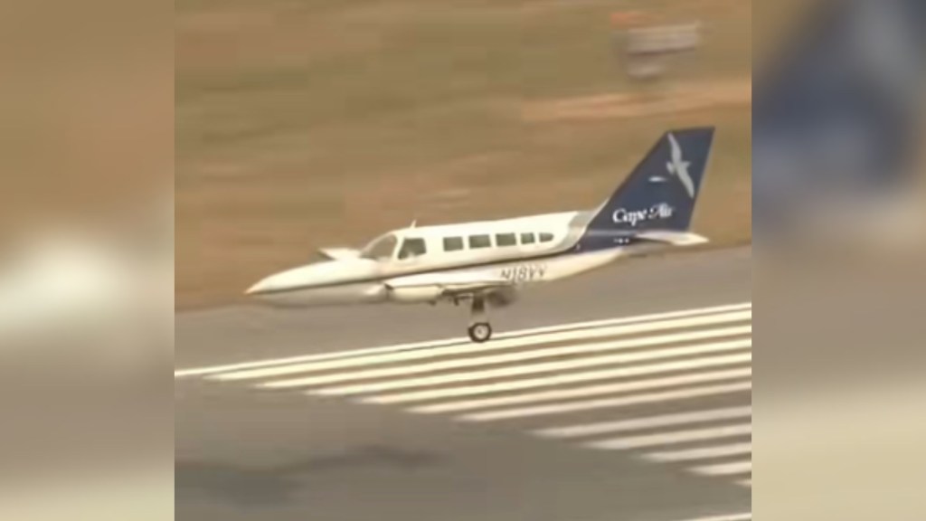 Distant view of a small airplane just about to land on a runway with only a single wheel