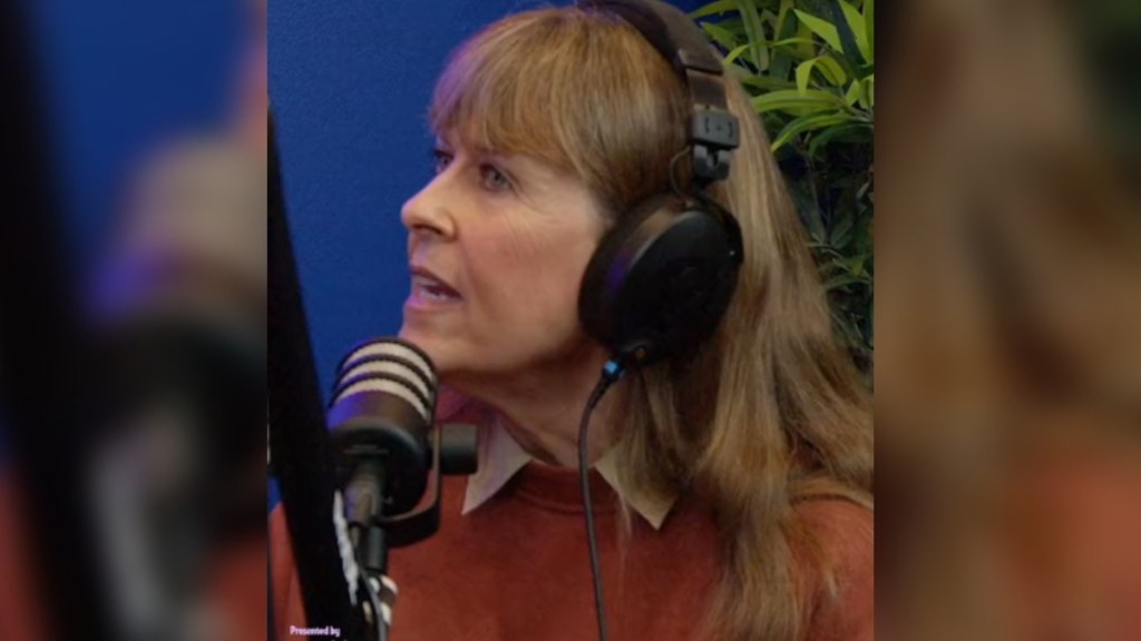 Terri Irwin looks to the side as she talks. She's wearing headphones and is talking into a podcast mic