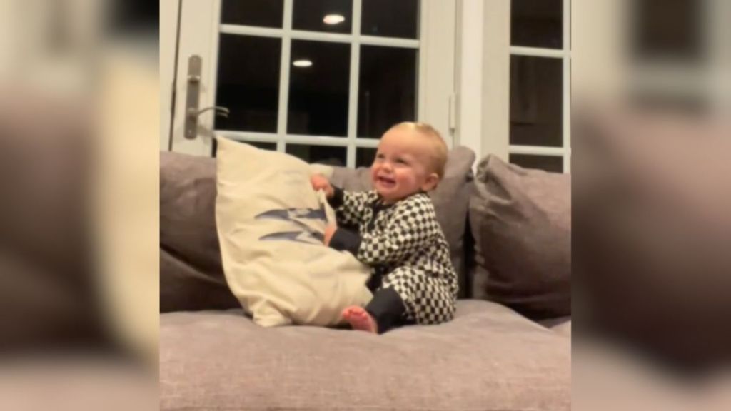 A baby holding a pillow and laughing.