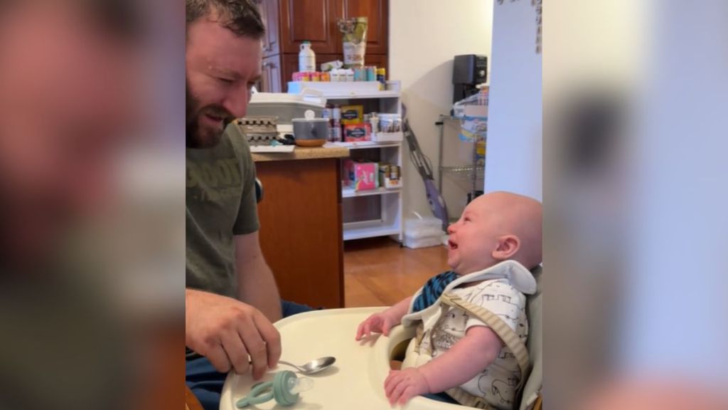 A baby in a high chair laughing with his dad.