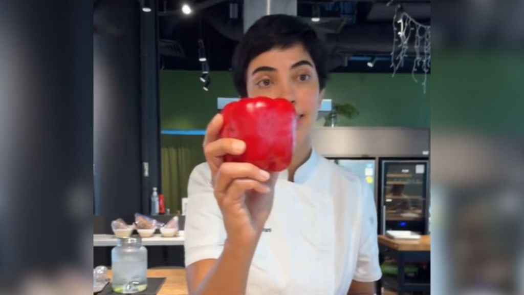 A chef holding up a red bell pepper.