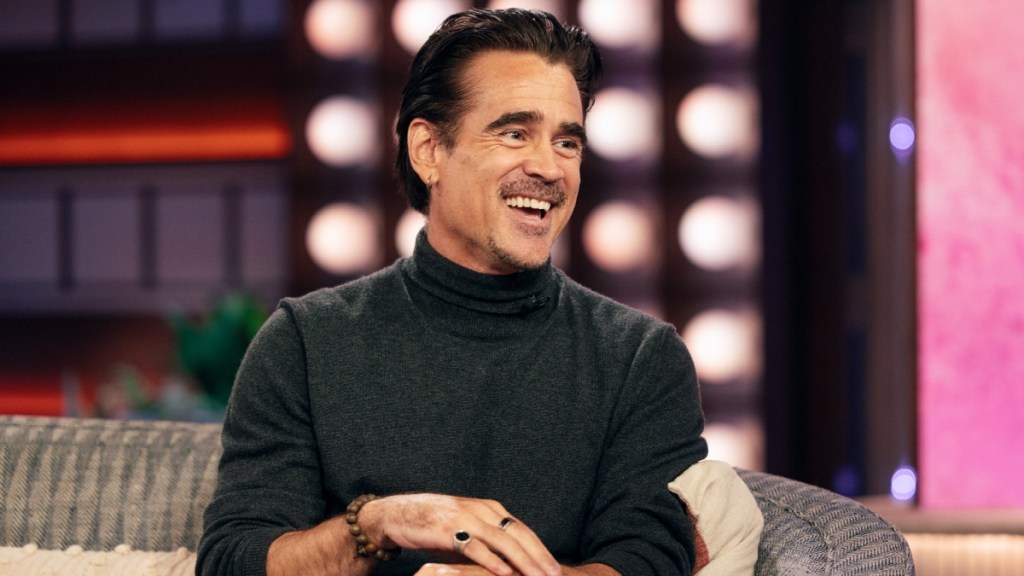 Colin Farrell smiles as he laughs. He sits on a couch.