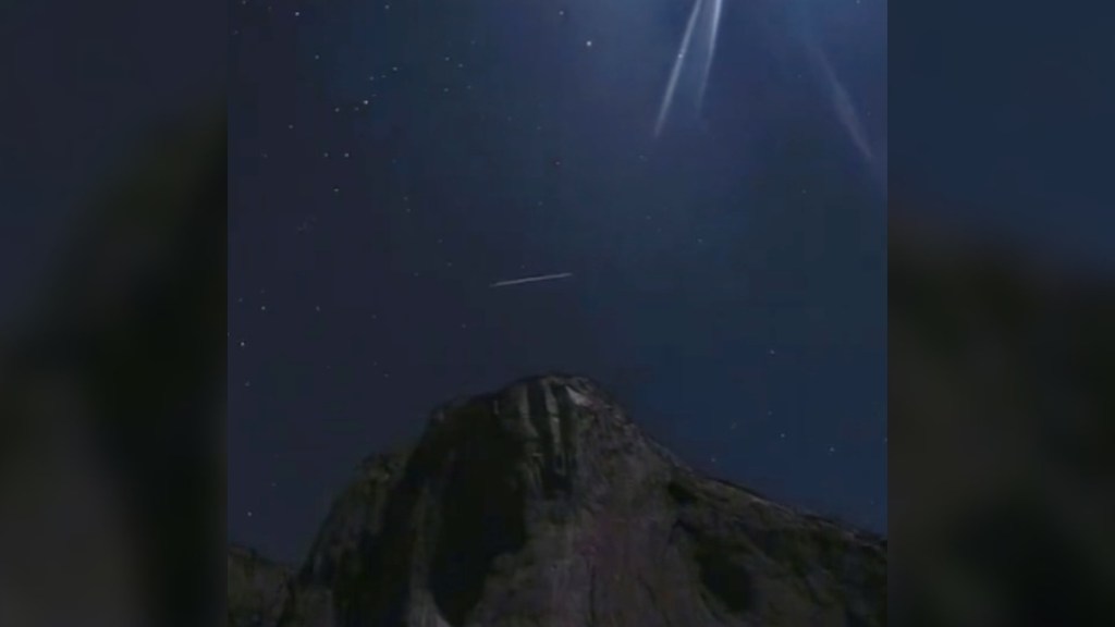 Night view of El Capitan at night. There's light shining through part of the sky as the dark blue sky starts to lighten