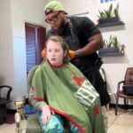 A barber putting a cape on the client in his chair.