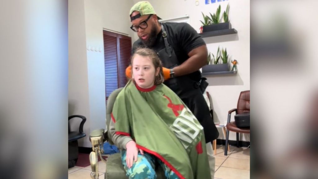 A barber putting a cape on the client in his chair.