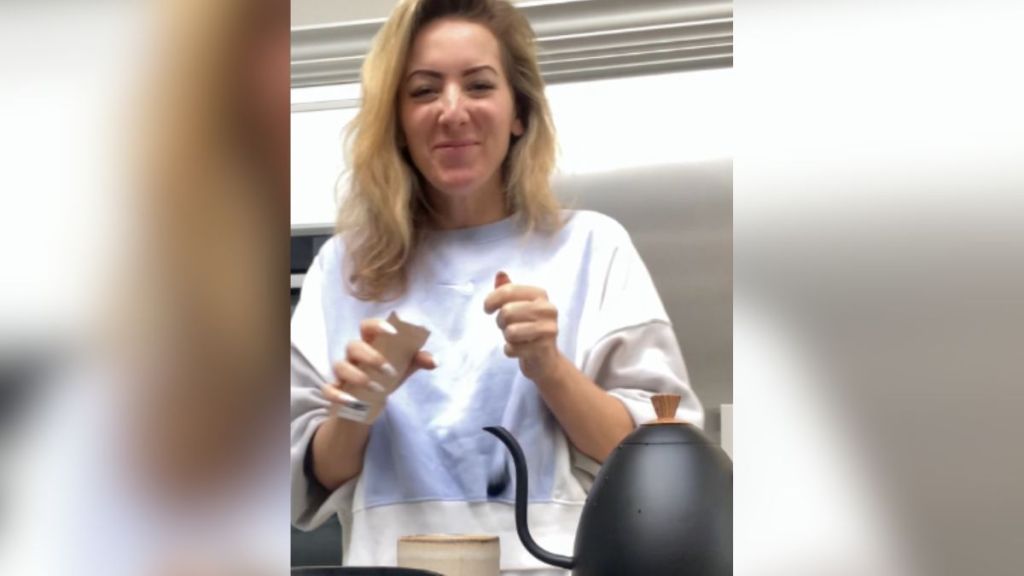 A blonde woman making tea and smiling.