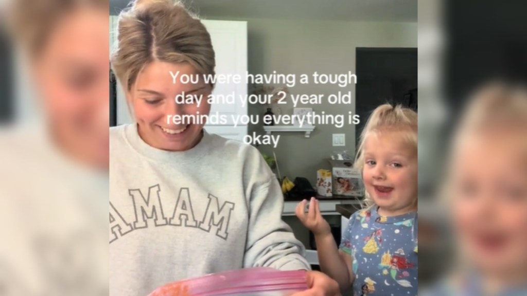 A woman smiles as she looks down at the bag in her hand. Her toddler smiles wide, looking into the camera. Text on the image reads: You were having a rough day and your 2 year old reminds you everything is okay