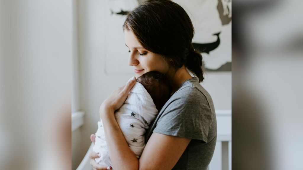 A mother holding a swaddled newborn baby.