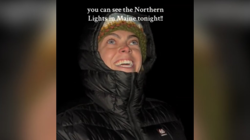 Close up of a woman looking up. She stand outside at night. Her eyes are wide and her mouth is wide open as she smiles. She's looking at something we can't see with awe. Text on the image reads: you can see the northern lights in Maine tonight!!