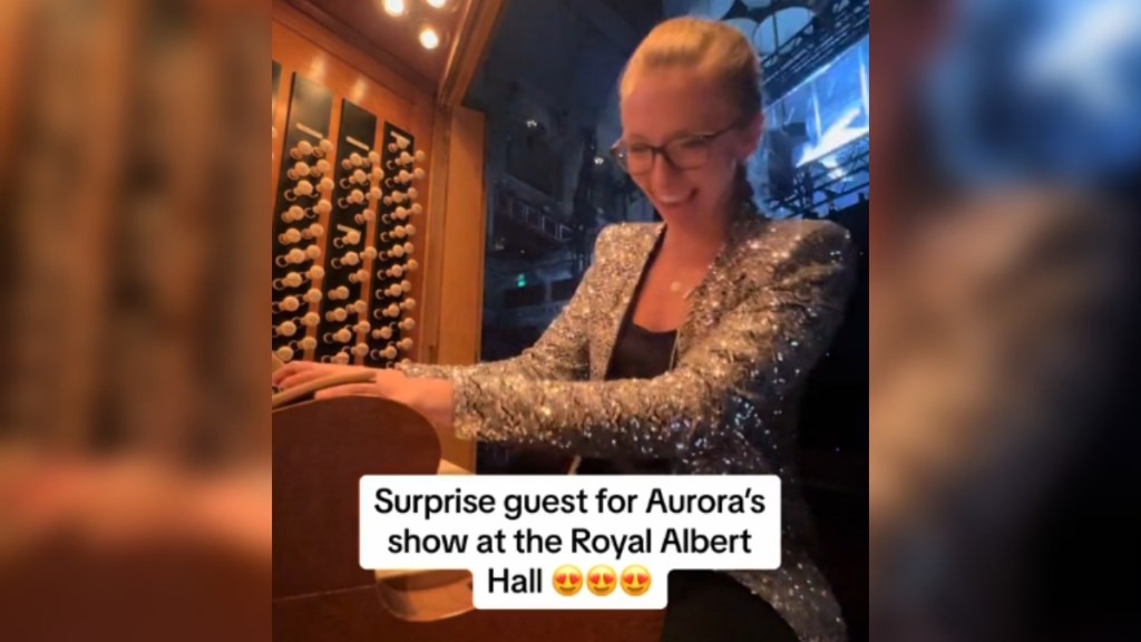 A woman smiles wide as she plays the organ. Text on the image reads: Surprise guest for AURORA's show at the Royal Albert Hall