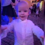 A toddler runs toward the camera, arms out to grab it.