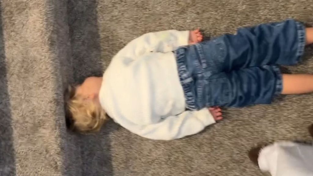 Image shows a toddler having a nap at the bottom of a carpeted stairway.