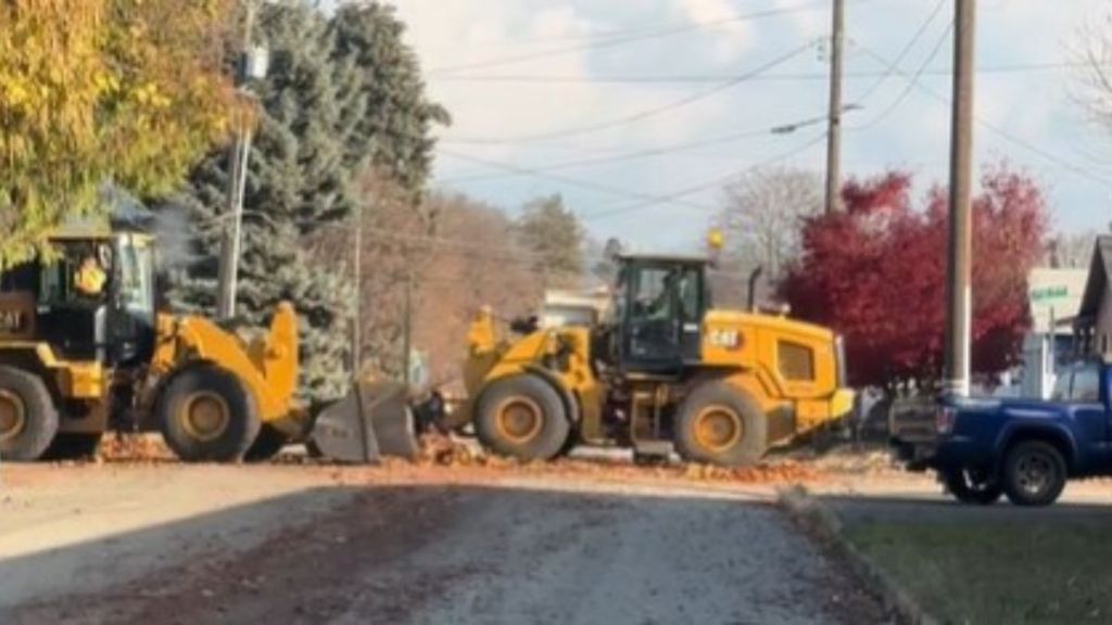 Image shows two tractors and a dump truck performing a ballet-like performance while doing bulk leaf pickup.