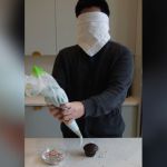 A blindfolded person decorating a cupcake.