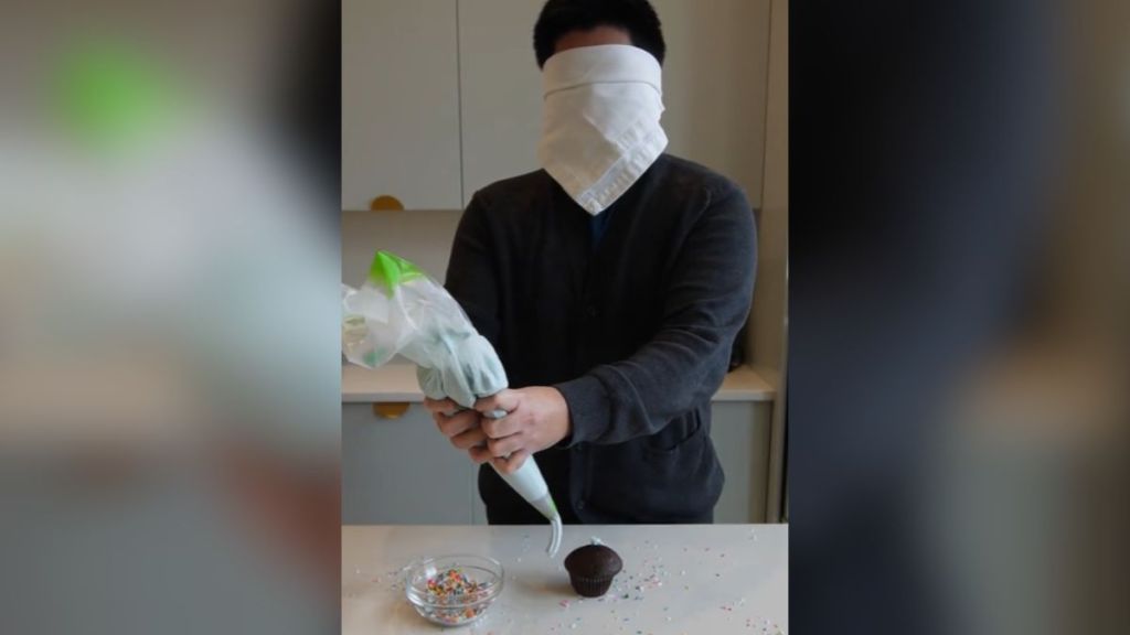 A blindfolded person decorating a cupcake.