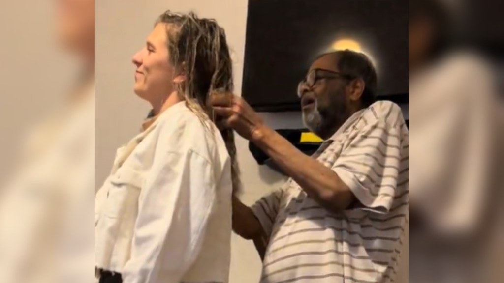 A man stands behind a woman, touching her hair.