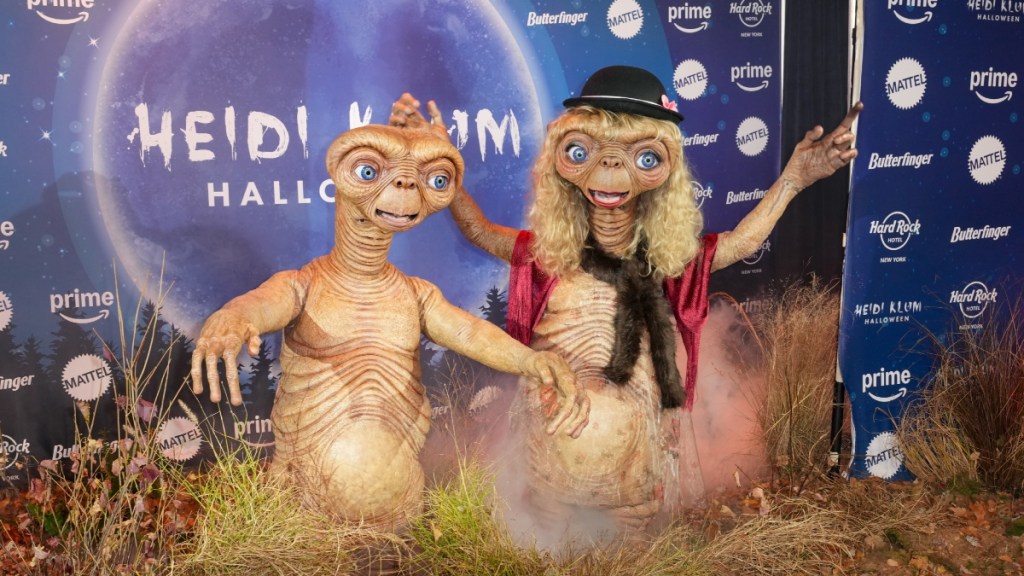 Tom Kaulitz and Heidi Klum pose for Klum's 2024 Halloween party. They're both dressed as two versions of E.T. Klum is dressed as E.T. in his blonde-wig look. If you look closely at their costumes' neck area, you can see Kaulitz and Klum's faces.