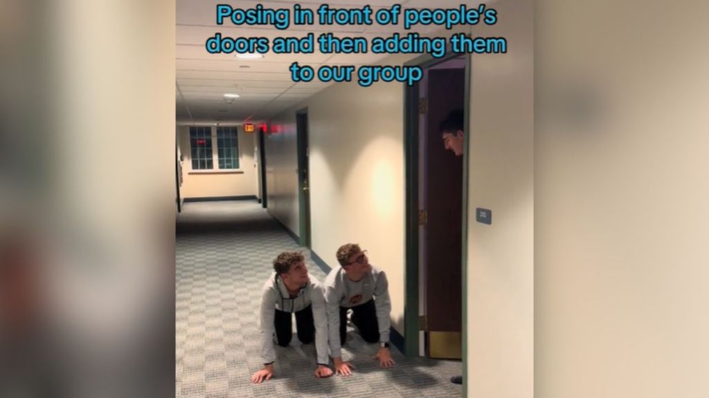 Two guys on their hands and knees outside someone else's dorm room.